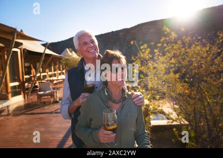 Happy senior couple drinking iced tea on sunny safari lodge balcony Stock Photo