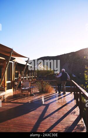 Affectionate senior couple hugging on sunny safari lodge balcony Stock Photo