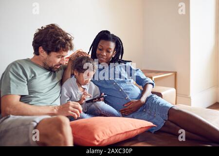 Young pregnant family using smart phone on living room sofa Stock Photo