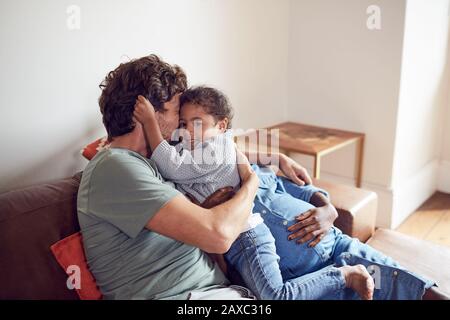 Affectionate young pregnant family cuddling on sofa Stock Photo