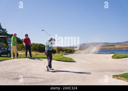 Man taking shot out of bunker on sunny golf course Stock Photo
