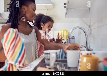 Mother and daughter washing dishes at kitchen sink Stock Photo