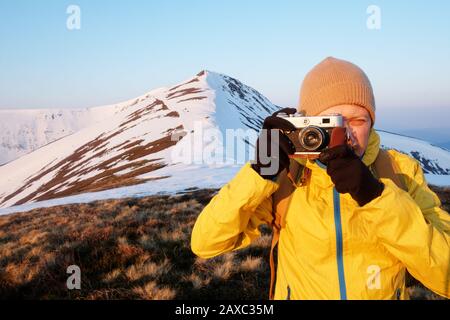 Photographer in yellow jacket taking photo on snowy winter field Stock Photo