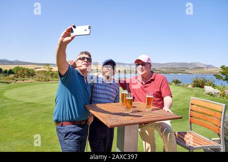 Male friends drinking beer and taking selfie on golf course patio Stock Photo