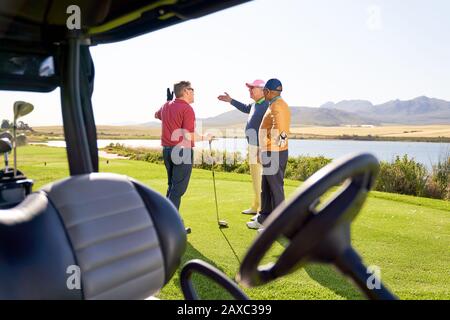 Male friends talking outside golf cart on sunny golf course Stock Photo