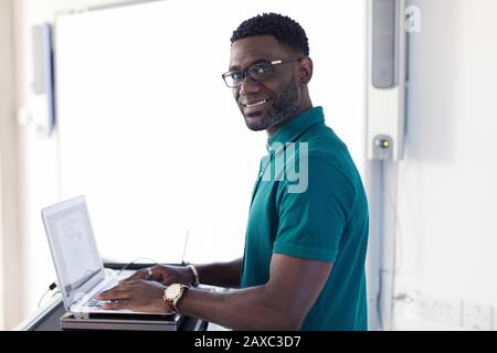 Portrait smiling, confident male instructor at laptop preparing in classroom Stock Photo