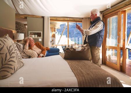 Senior man with camera phone photographing wife on hotel bed Stock Photo