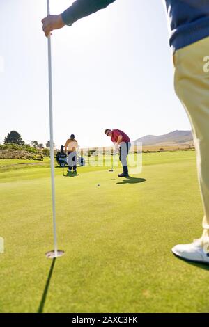 Male golfer putting towards pin and hole on sunny golf course Stock Photo