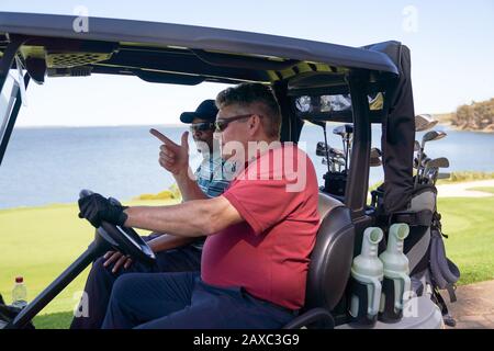 Male golfers driving golf cart on lakeside golf course Stock Photo