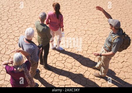 Safari tour guide talking with group on sunny cracked earth Stock Photo