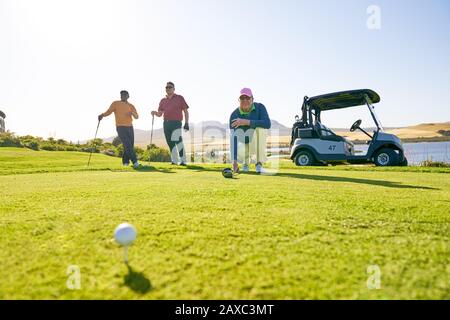 Male golfers preparing to tee off at sunny tee box Stock Photo
