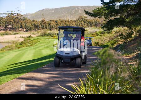 Male golfers riding in golf cart on sunny golf course path Stock Photo
