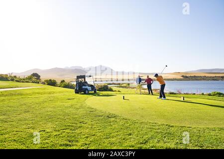 Male golfer teeing off at sunny lakeside tee box Stock Photo