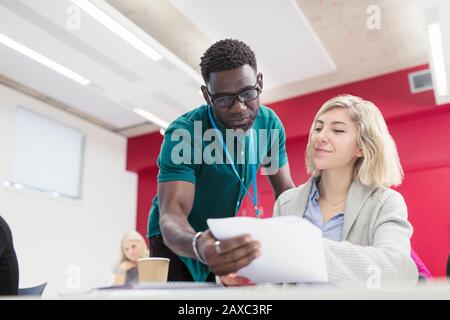 Community college instructor helping student with paperwork in classroom Stock Photo