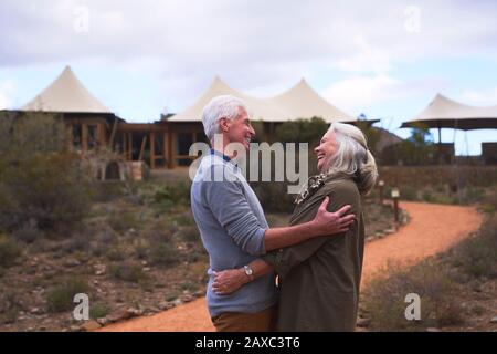 Affectionate senior couple hugging outside safari lodge hotel Stock Photo