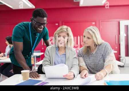 Community college instructor helping students with paperwork in classroom Stock Photo
