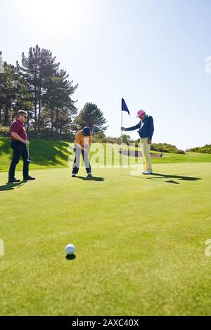 Male golfer putting at hole on sunny golf course putting green Stock Photo