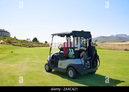 Male golfers driving golf cart on sunny golf course greens Stock Photo