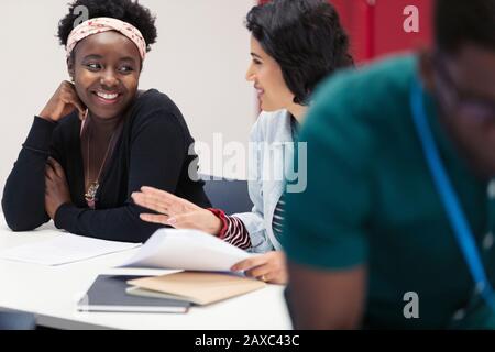 Smiling female community college students discussing paperwork in classroom Stock Photo