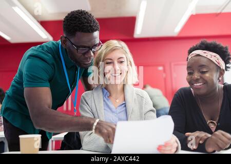 Community college instructor helping students with paperwork in classroom Stock Photo