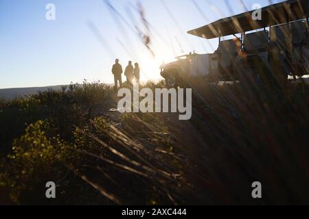 Silhouette safari tour group and off-road vehicle on hill at sunrise Stock Photo