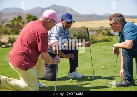 Male golfers kneeling and talking on sunny practice putting green Stock Photo