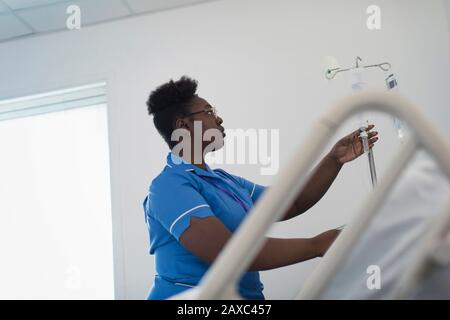 Female nurse adjusting IV drip in hospital room Stock Photo