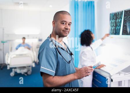Portrait confident, smiling doctor using digital tablet in hospital room Stock Photo