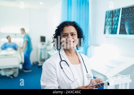Portrait smiling, confident female doctor using digital tablet in hospital room Stock Photo