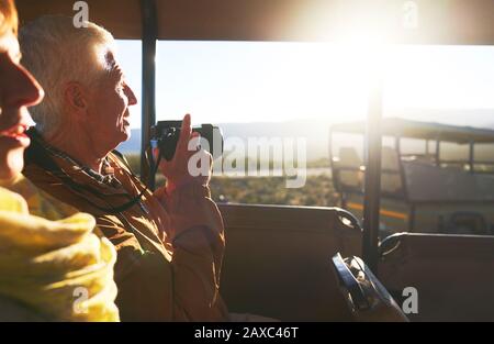Senior couple with digital camera riding in safari off-road vehicle Stock Photo