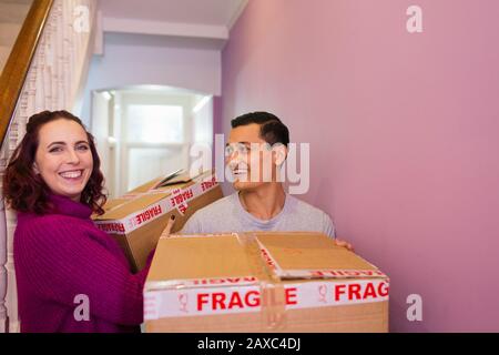 Portrait happy couple moving house, carrying cardboard boxes in corridor Stock Photo