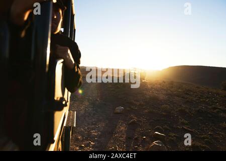 Safari off-road vehicles driving along rock dirt road at sunrise Stock Photo