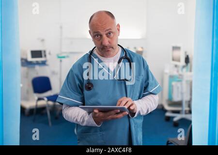 Portrait confident, serious male doctor using digital tablet in hospital room Stock Photo