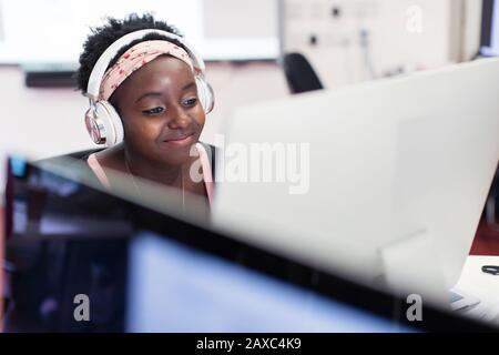 Smiling female community college student with headphones at computer in classroom Stock Photo