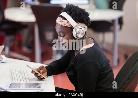 Female student with headphones using smart phone in classroom Stock Photo