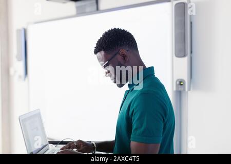 Male professor using laptop next to projection screen in classroom Stock Photo