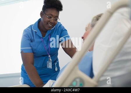 Smiling, caring female nurse talking with patient in hospital bed Stock Photo