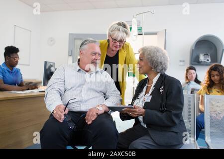 Doctor with digital tablet talking to couple in clinic lobby Stock Photo