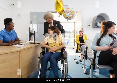 Female receptionist greeting girl patient in wheelchair in clinic Stock Photo