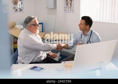 Male doctor shaking hands with senior patient in doctors office Stock Photo