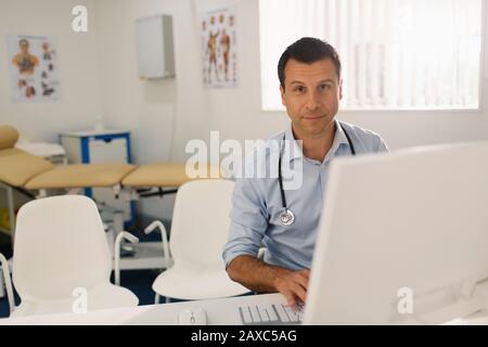 Portrait confident male doctor working at computer in doctors office Stock Photo