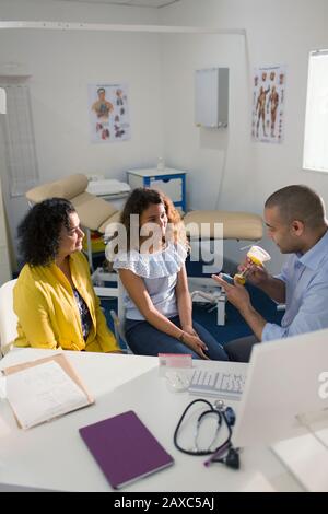 Male doctor explaining inhaler to mother and daughter in doctors office Stock Photo