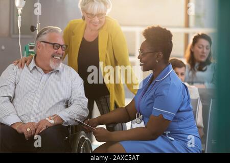 Female nurse talking with senior male patient in wheelchair in clinic lobby Stock Photo