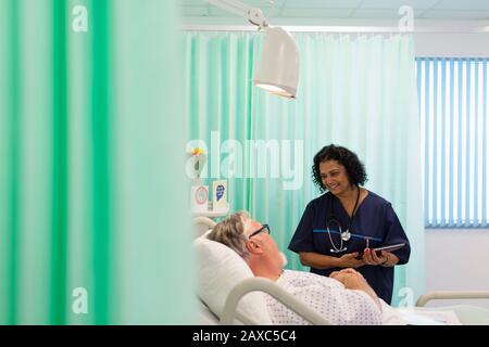 Doctor with digital tablet making rounds, talking with senior patient in hospital room Stock Photo