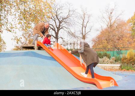 Grandparents playing with grandson on playground slide Stock Photo