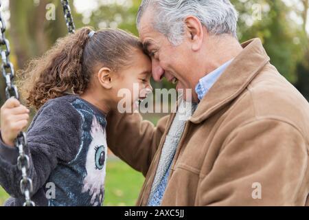 Playful affectionate grandfather and granddaughter on swing at playground Stock Photo