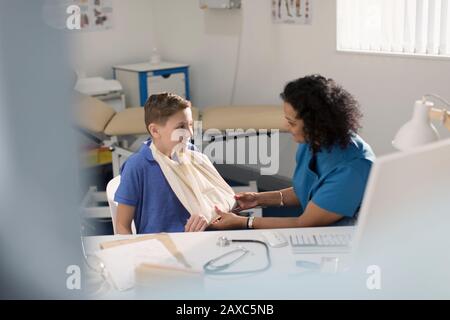 Female doctor checking arm sling of boy patient in doctors office Stock Photo
