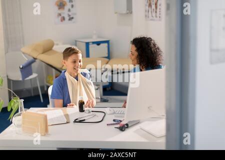 Female pediatrician talking to boy patient with arm in sling in doctors office Stock Photo