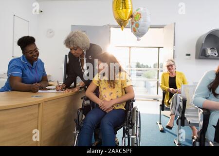 Girl patient in wheelchair checking in at clinic reception Stock Photo