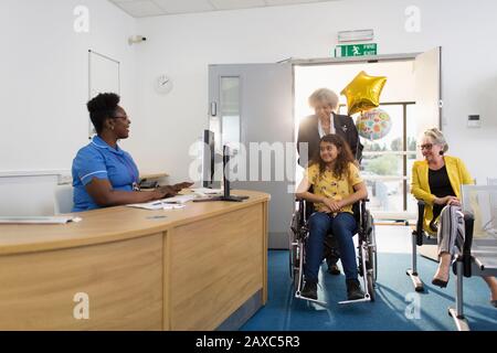 Woman pushing girl patient in wheelchair into clinic reception Stock Photo
